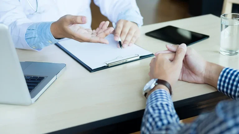 Médico e paciente estão discutindo algo, apenas as mãos na mesa