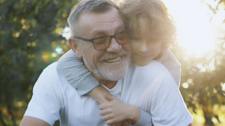 Homem idoso abraçado ao seu neto em um parque 