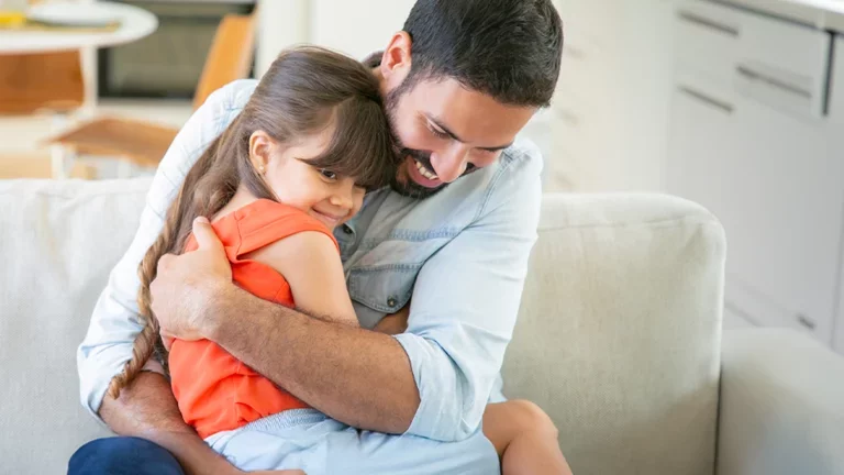 Pai e filha sentados no sofá abraçados.