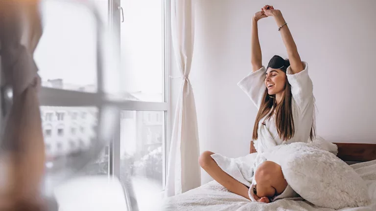 Mulher acordando disposta em sua casa fazendo um alongamento 
