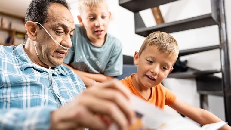 Homem com cateter de oxigênio lendo um livro com seus netos