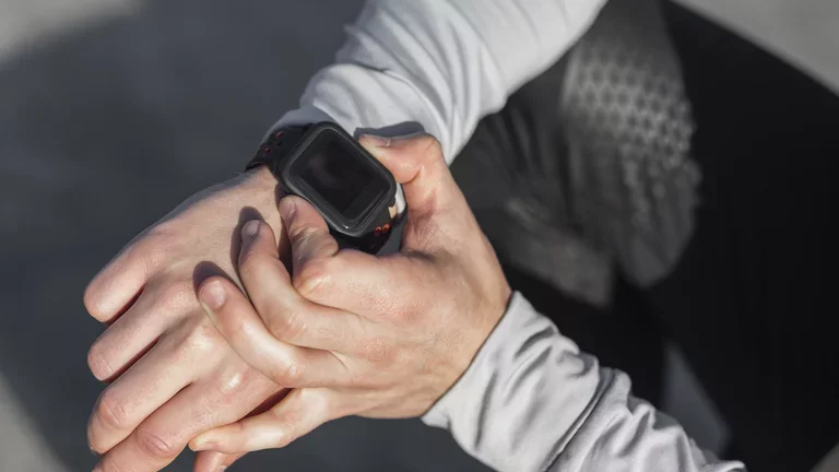 Homem avaliando seu smartwatch após acordar sentado na cama