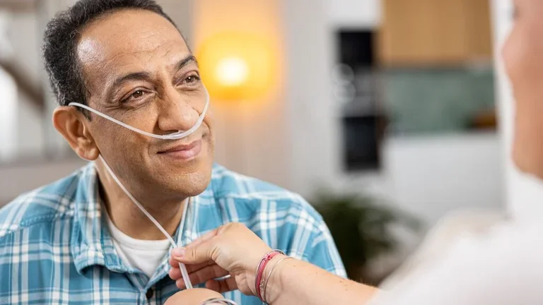 Homem sorrindo para a cuidadora que está ajustando o catéter nasal