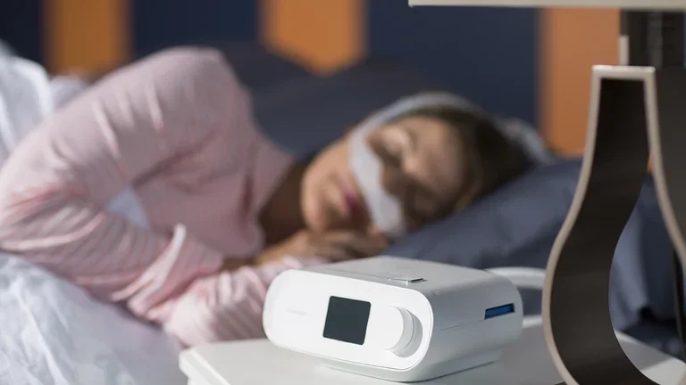 Mulher dormindo com CPAP DreamStation e Máscara DreamWear em sua cama confortavelmente