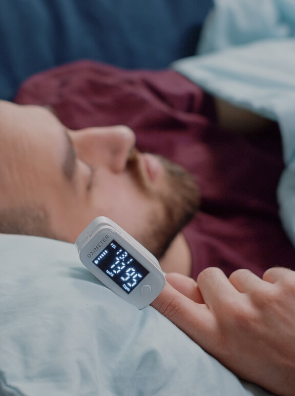 Homem deitado utilizando oxímetro de dedo