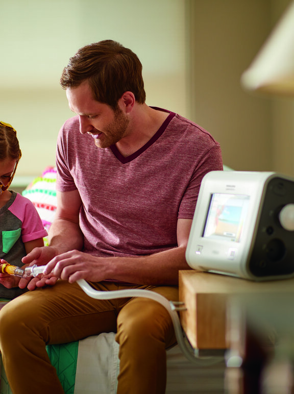 Criança em ventilação mecânica não-invasiva sentada ao lado do pai