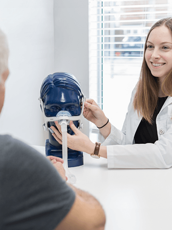 Consultora de Terapia Respiratória apresentando um modelo de máscara nasal ao paciente