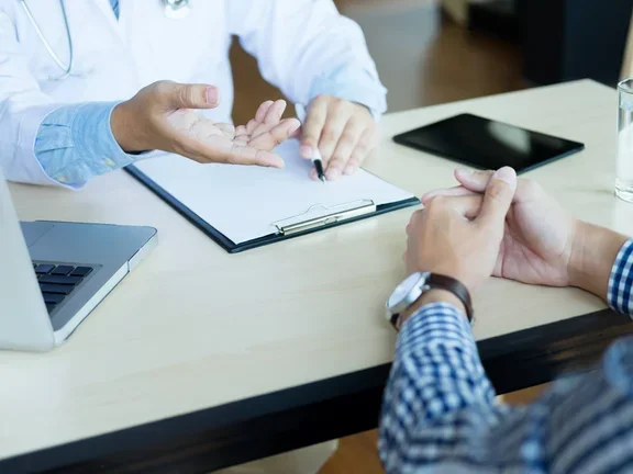 Médico e paciente estão discutindo algo, apenas as mãos na mesa