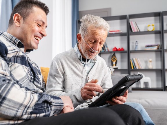 Homem idoso com cateter de oxigênio acessando o tablet de um jovem para informações