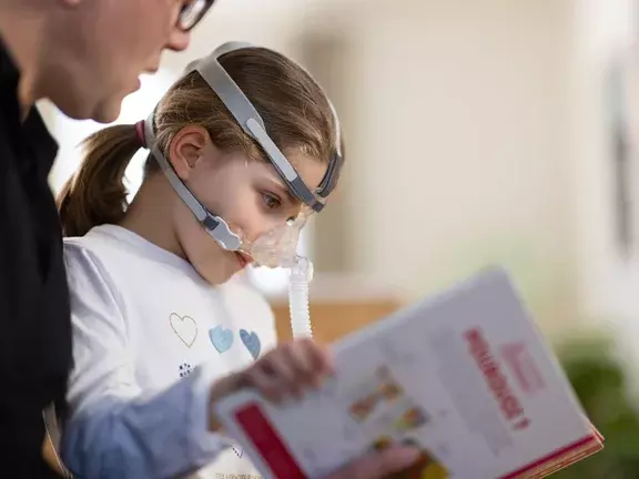 Criança em ventilação mecânica não invasiva lendo um livro infantil