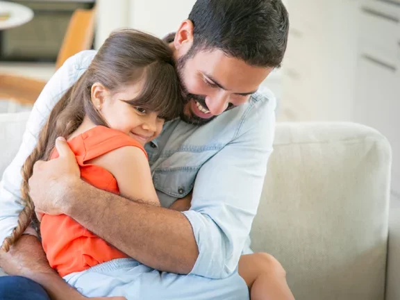 Pai e filha sentados no sofá abraçados.