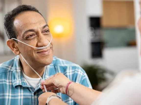 Homem sorrindo para a cuidadora que está ajustando o catéter nasal