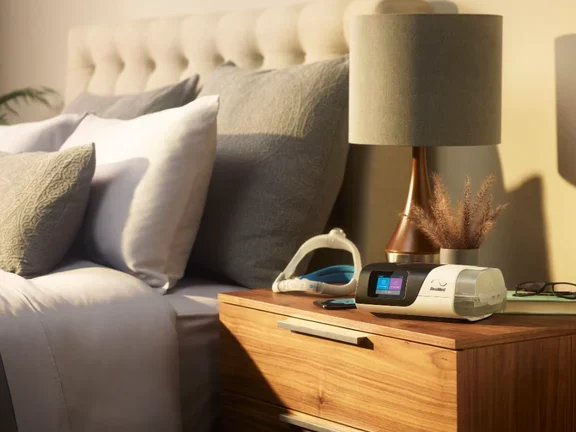 Imagem de um quarto com o CPAP Airsense S11 Resmed e máscara destacada no armário de canto