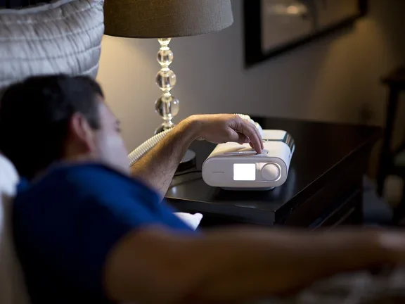 Homem deitado na cama verificando o ajuste do CPAP