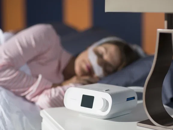 Mulher dormindo com CPAP DreamStation e Máscara DreamWear em sua cama confortavelmente