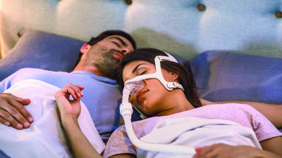 Homem e mulher dormindo com CPAP em casa