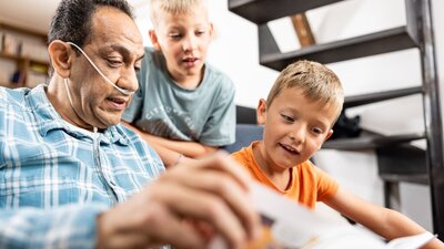 Homem com cateter de oxigênio lendo um livro com seus netos