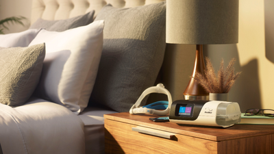 Imagem de um quarto com o CPAP Airsense S11 Resmed e máscara destacada no armário de canto
