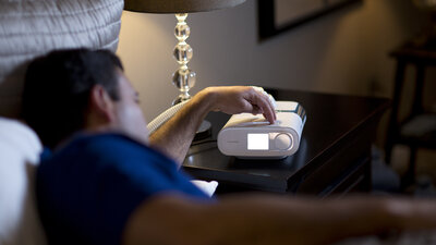 Homem deitado na cama verificando o ajuste do CPAP