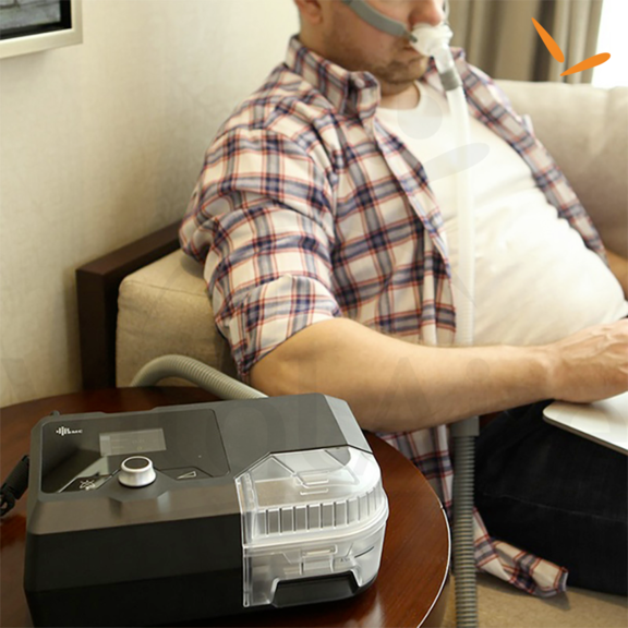 Homem sentado no sofá com o sua máscara de CPAP conectada