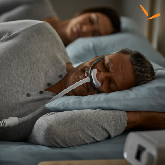 Homem dormindo com máscara de CPAP ao lado de sua parceira
