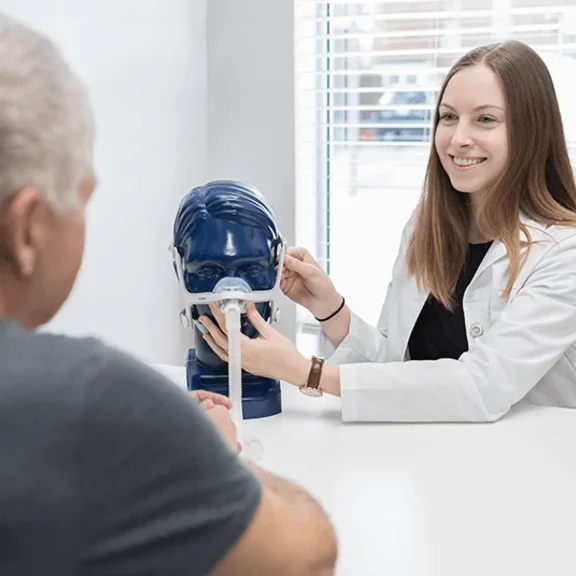 Consultora de Terapia Respiratória apresentando um modelo de máscara nasal ao paciente