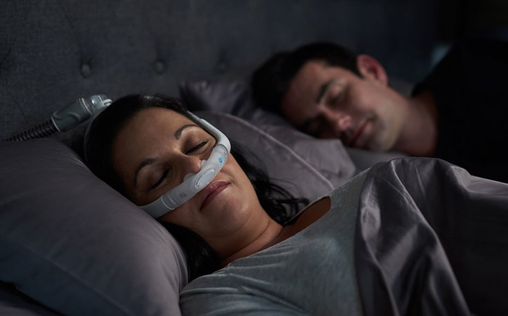 Mulher dormindo com CPAP acompanhada do marido