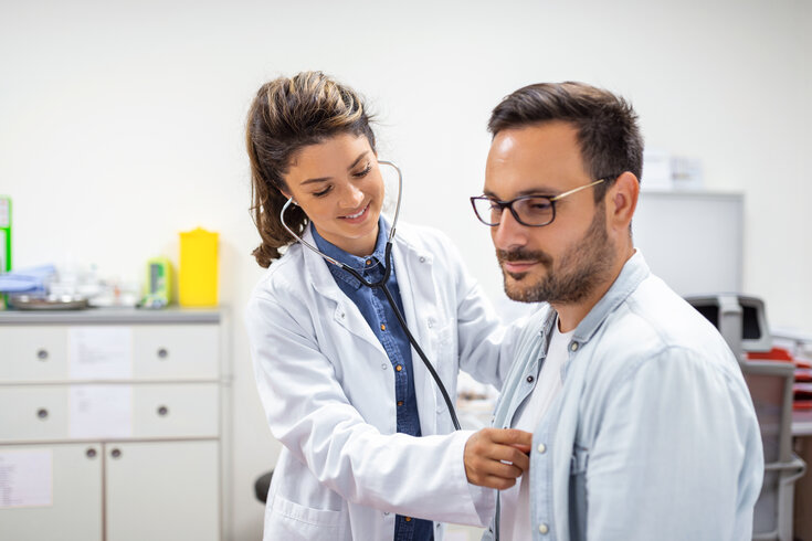 Médica usando um estetoscópio para examinar o pulmão e os batimentos cardíacos do paciente sentado na maca.