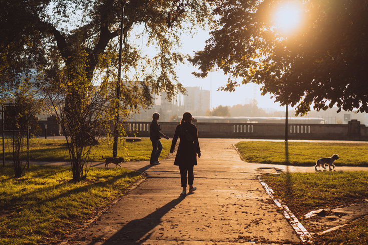 Imagem de um parque com pessoas caminhando ao pôr do sol.