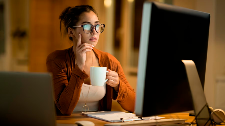 Mulher trabalhando em frente ao computador até tarde ingerindo café