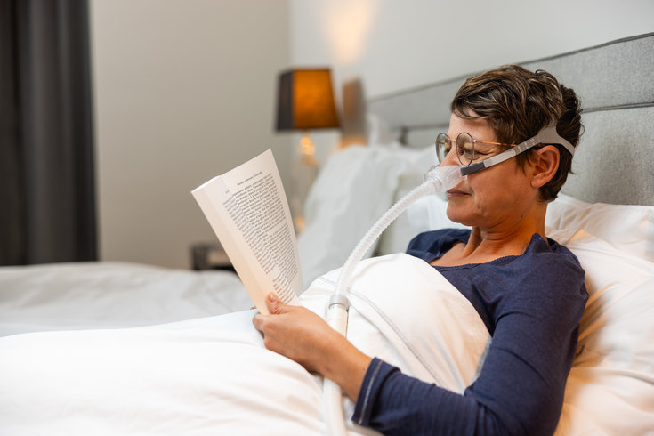 Mulher lendo sentada em sua cama com a Máscara Nasal Alnest MC1