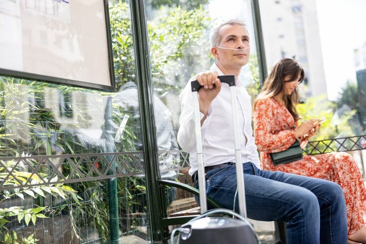 Homem em uso de oxigênio aguardando o ônibus.