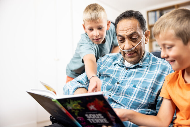 Homem dependente de oxigênio lendo um livro para os netos em sua casa